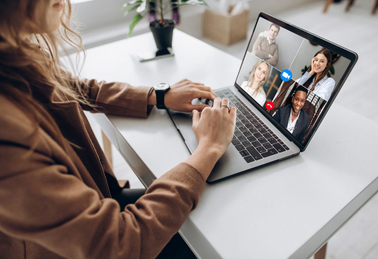 A person typing on a laptop during a video call with multiple participants displayed on the screen, sitting at a bright caribbean jobs online workspace.